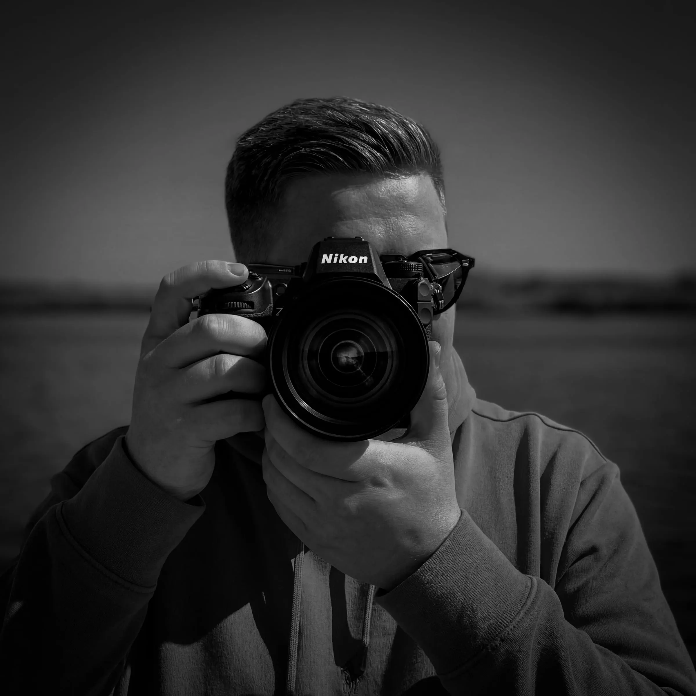 Christopher Gawollek mit Nikon-Kamera vor dem Gesicht, Schwarz-Weiß