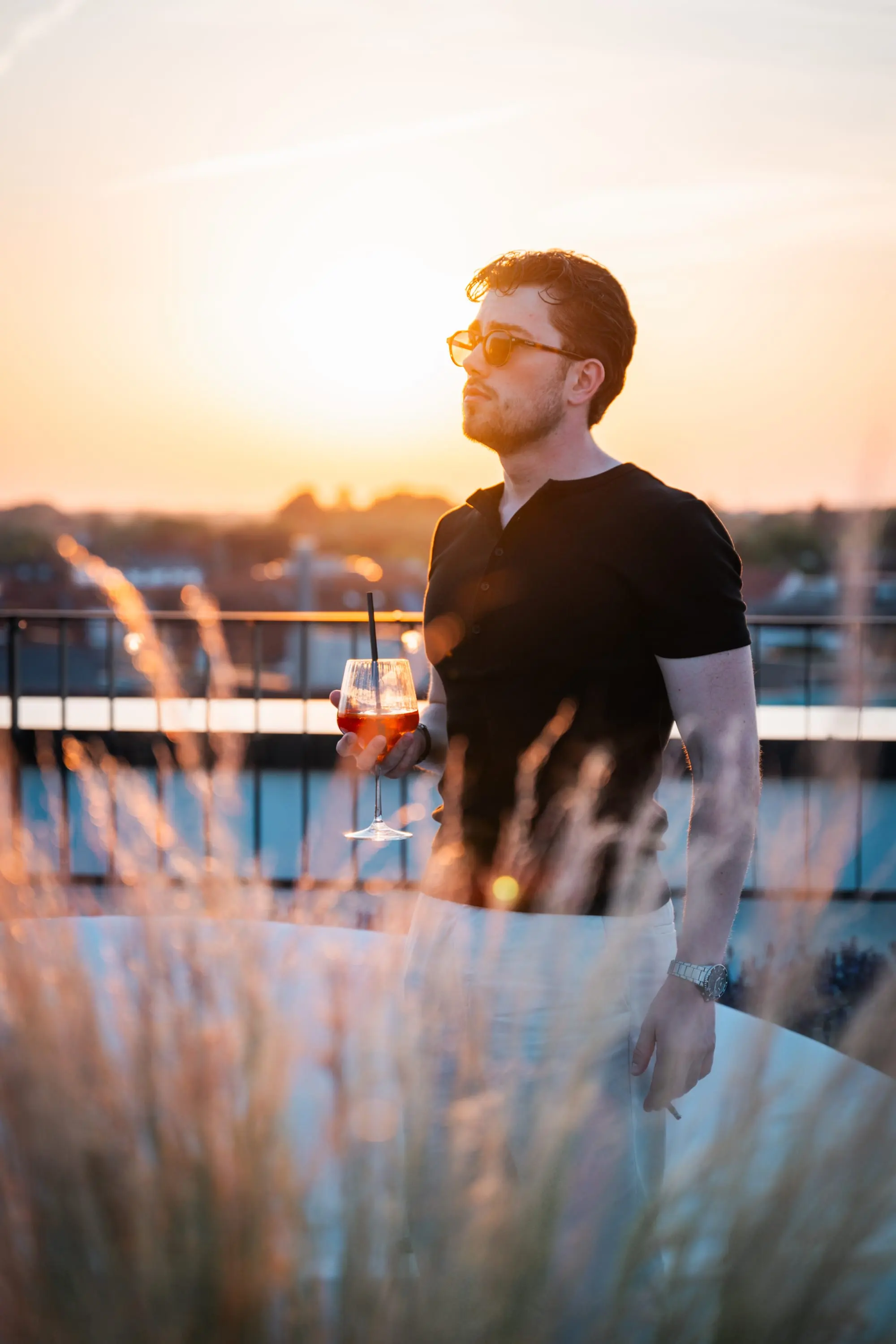 Mann mit Drink auf einer Dachterrasse im Sonnenuntergang
